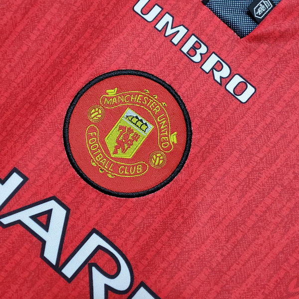 camisa-manchester-united-retrô-titular-1-home-1996-vermelho-preto-gola-polo-manga-curta-fundo-branco-pendurada-cabide-botão