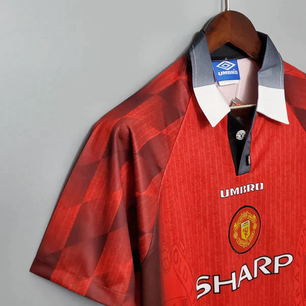 camisa-manchester-united-retrô-titular-1-home-1996-vermelho-preto-gola-polo-manga-curta-fundo-branco-pendurada-cabide-lateral